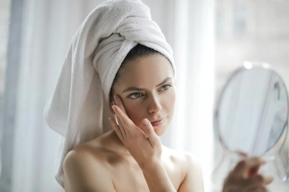 Woman examining skin in mirror — copper peptide GHK-Cu and collagen research peptides for skin health